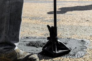 person filling a driveway pothole with cold asphalt patch
